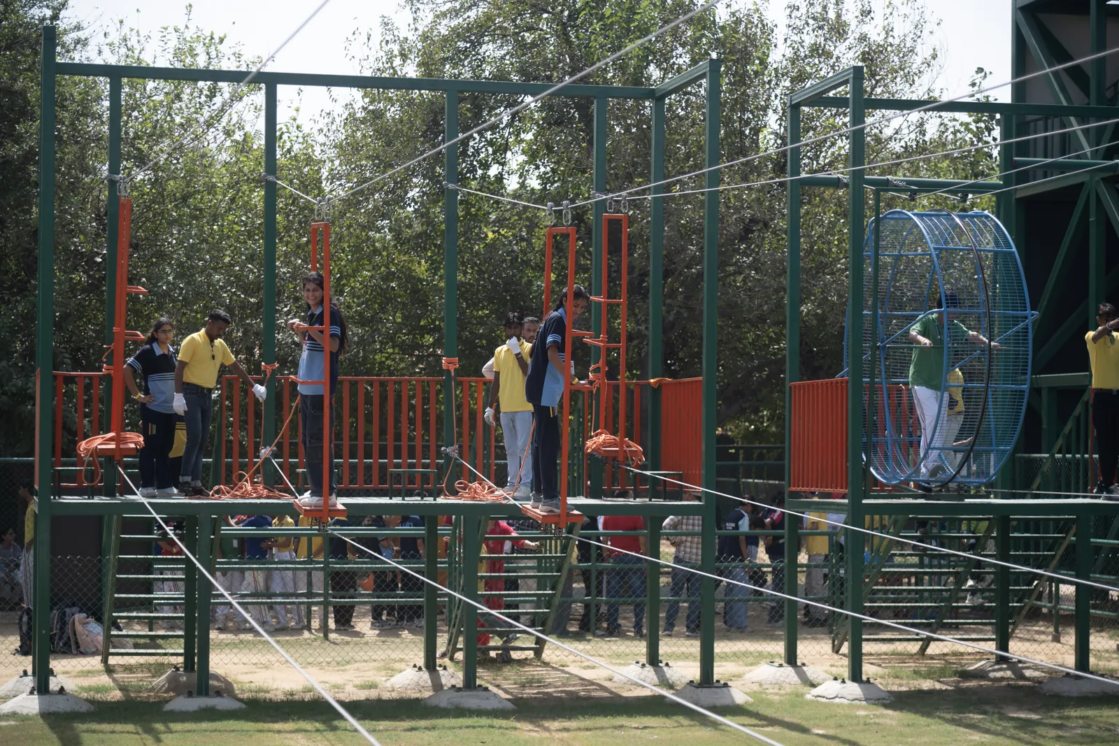 Guests in harnesses on the adventure course, with ziplines strung overhead and the sky cycling cage beside them