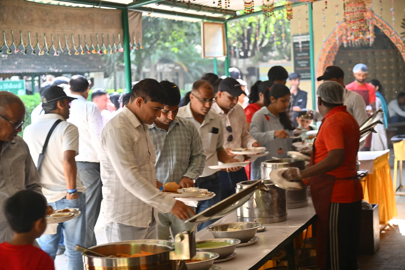 Guests queuing with plates at the unlimited food counter while staff in gloves and caps serve from steaming handis