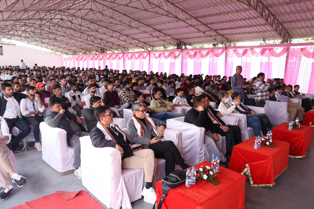 A large corporate audience seated in rows of white-covered chairs inside the covered hall