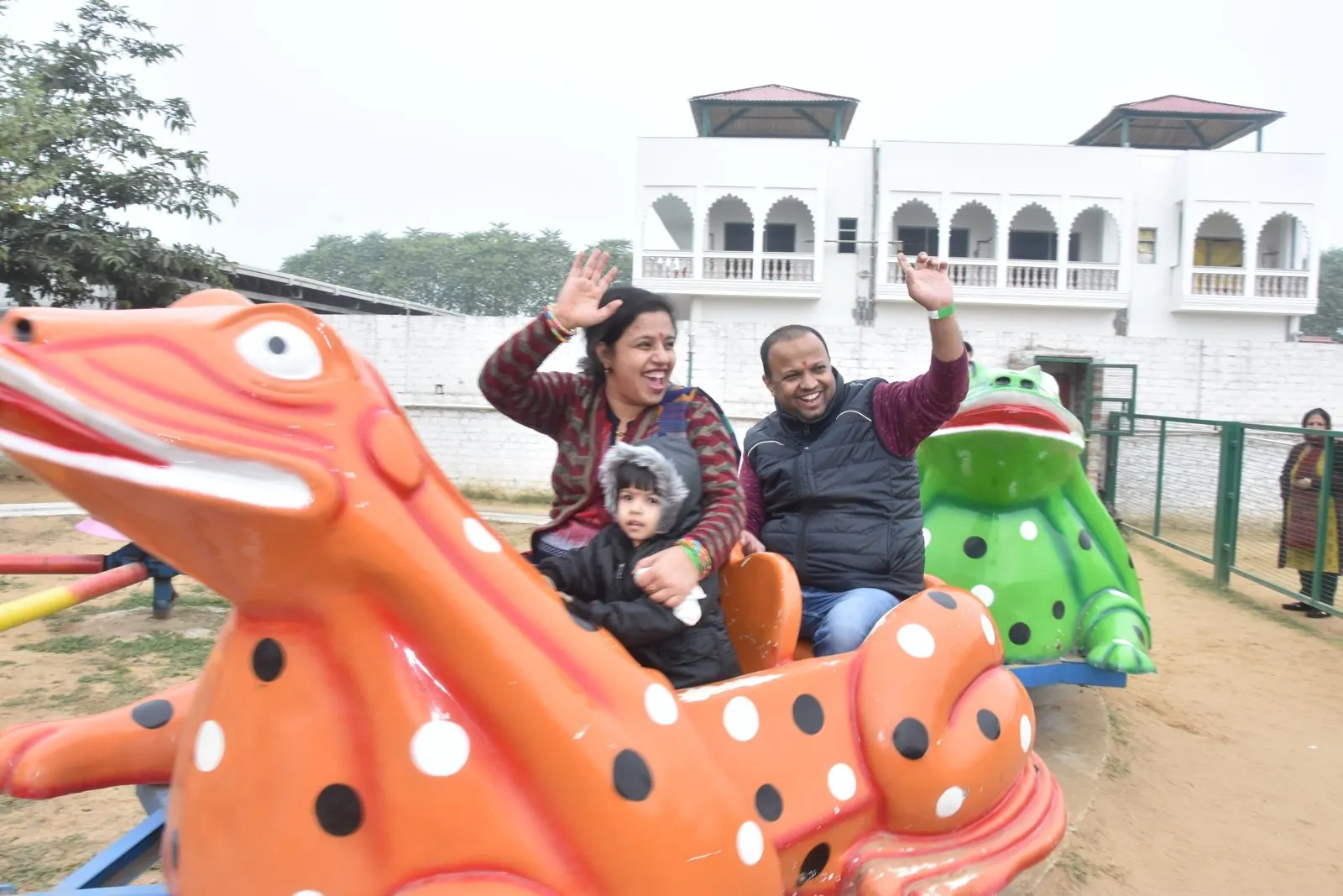 A couple and a small child riding a painted frog on the fun rides with their hands raised