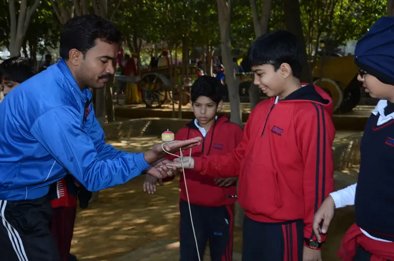 Instructor in a blue track jacket showing students a spinning top balanced on his palm